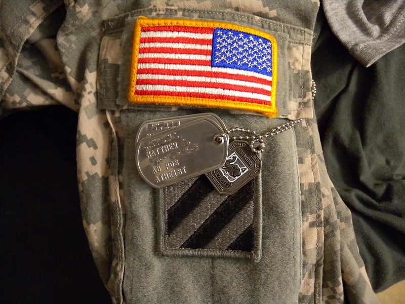Dog tags sitting by the American flag on a military outfit.