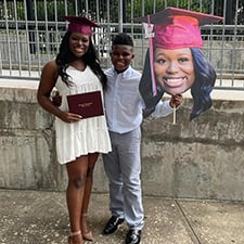 Graduate next to her loved one, holding a cardboard cutout of her head.