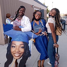 Graduate holding her diploma with her friends and BigHead cutout.