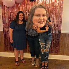 Women holding cardboard head cutout at graduation party